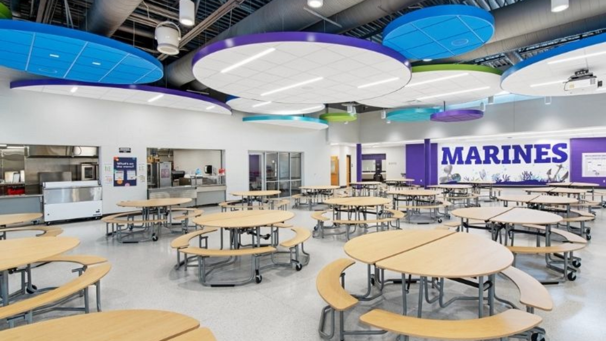 School cafeteria with mobile round tables, attached benches, and colorful acoustic ceiling panels